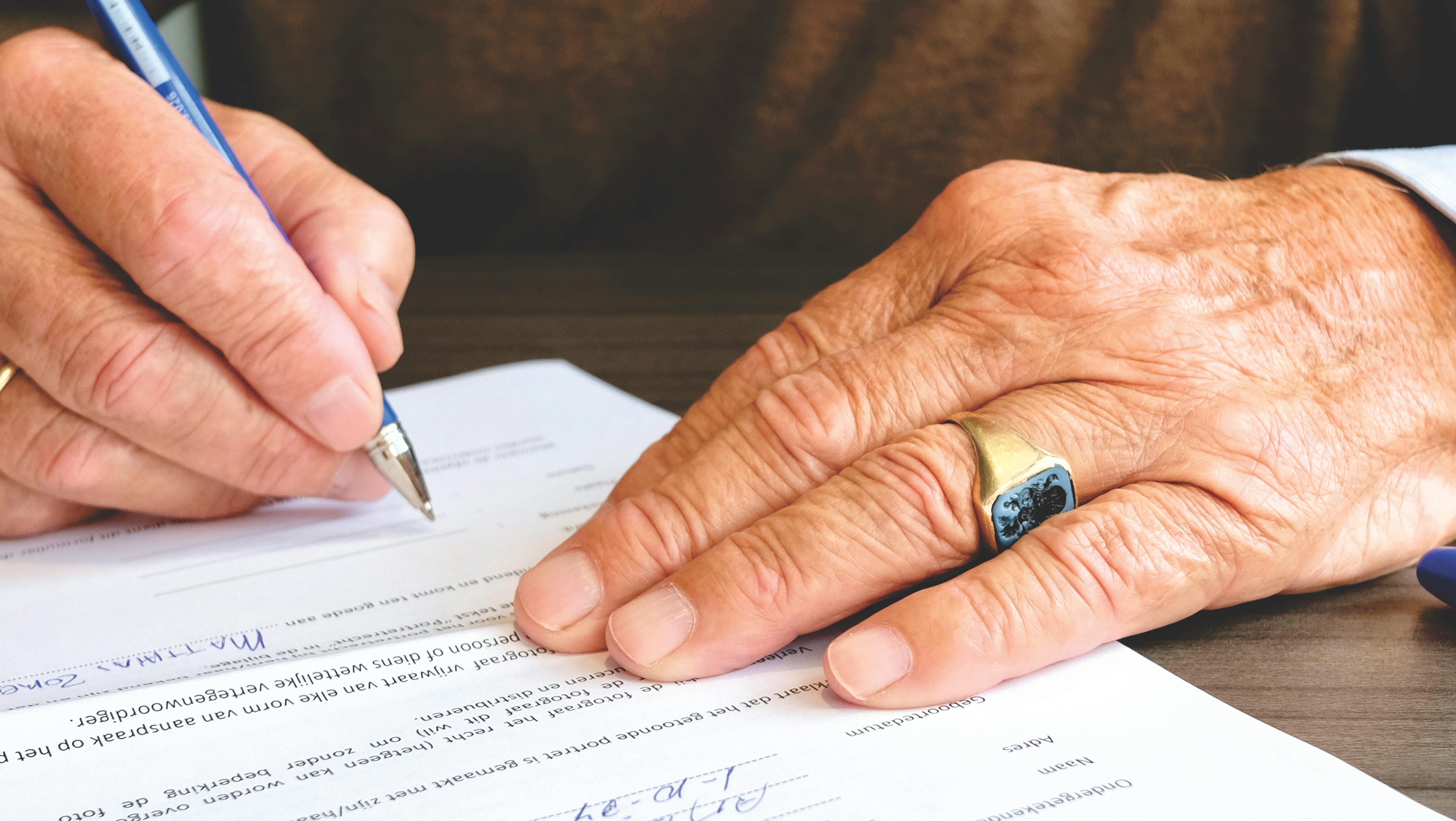 elderly man's hands signing a document