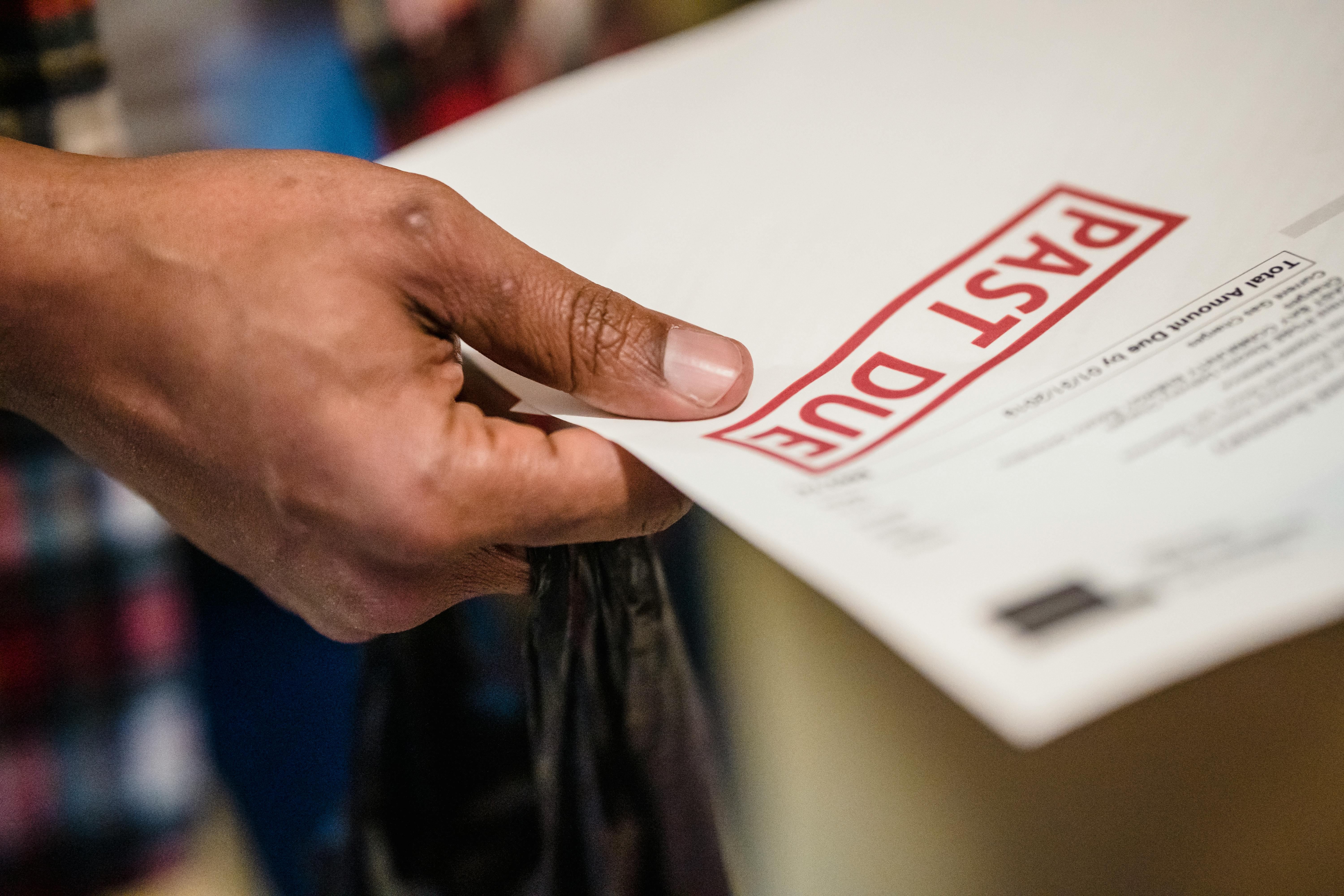 a hand holding a letter that is stamped with "past due" in red